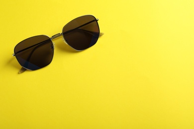 Stylish sunglasses on yellow background, top view. Space for text