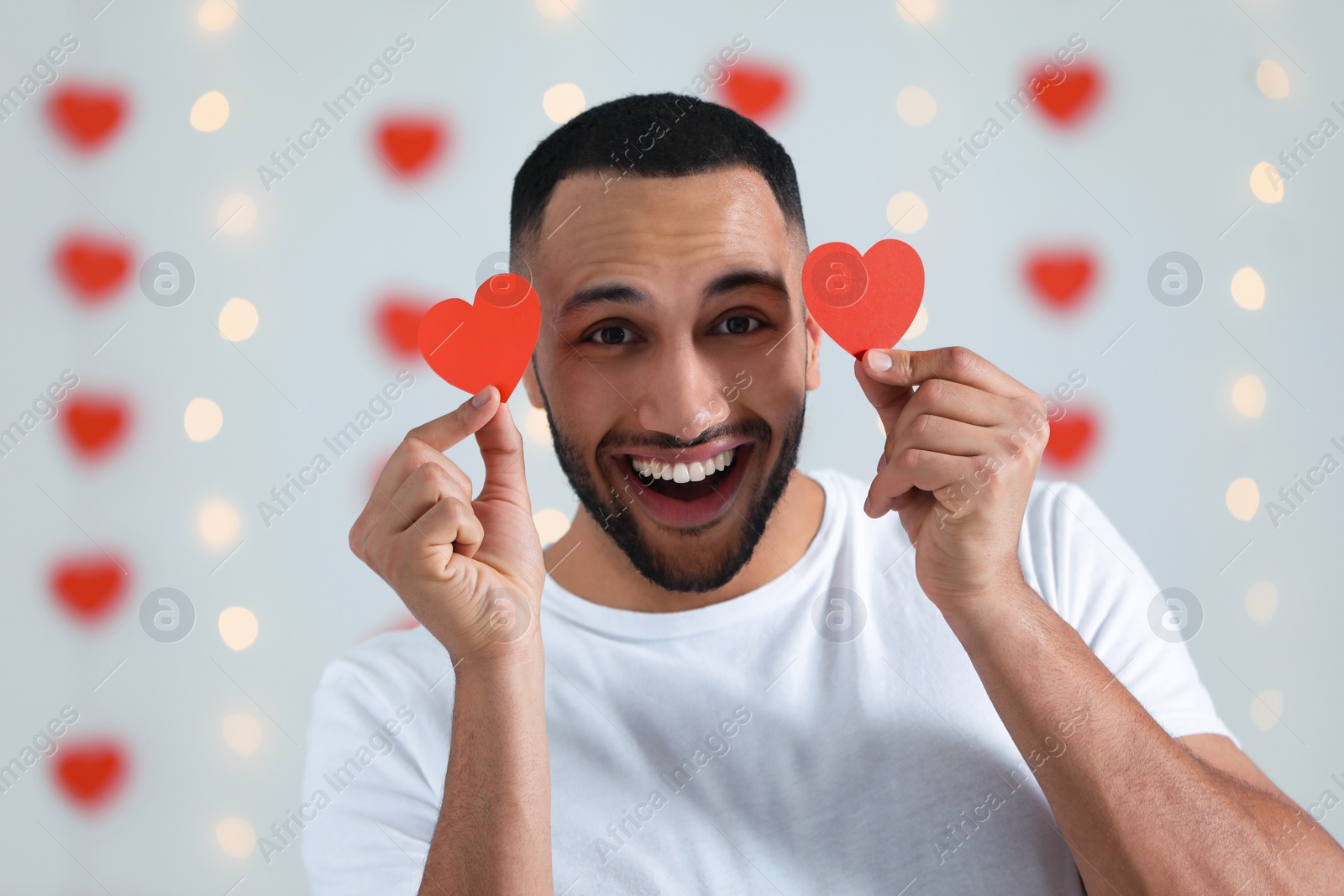 Photo of Handsome young man with red paper hearts indoors, view from camera. Valentine's day celebration in long distance relationship