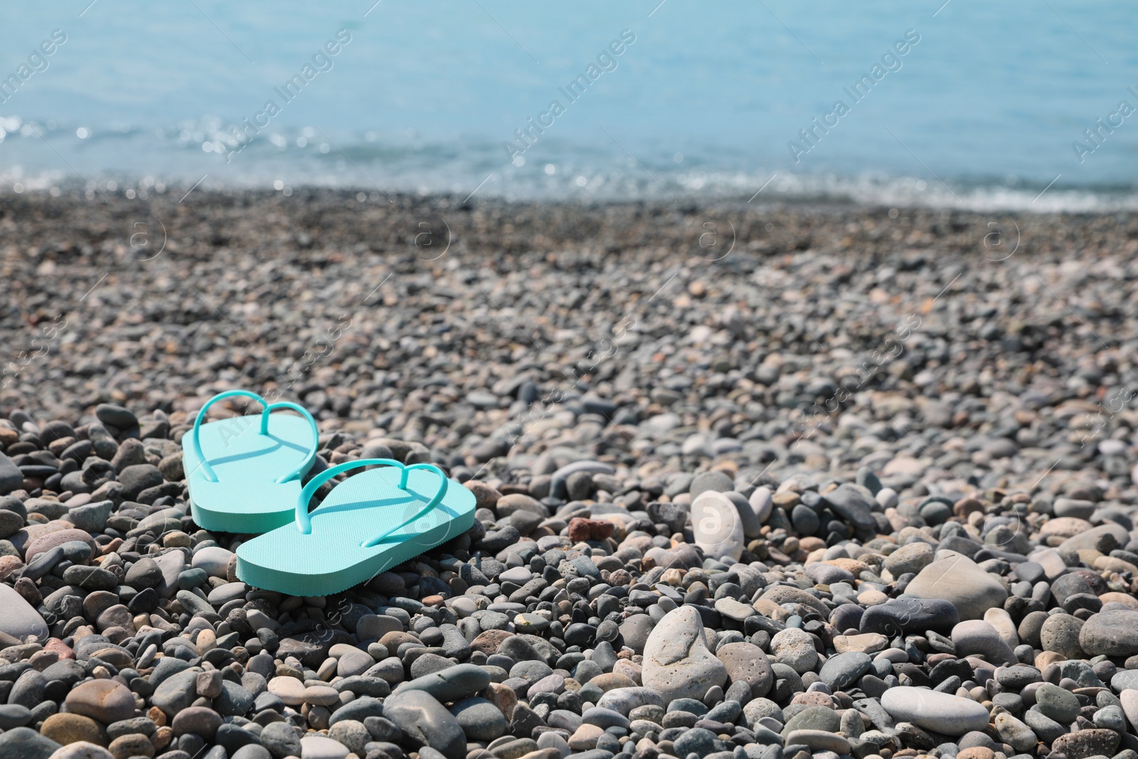 Photo of Stylish turquoise flip lops on pebble beach near sea. Space for text