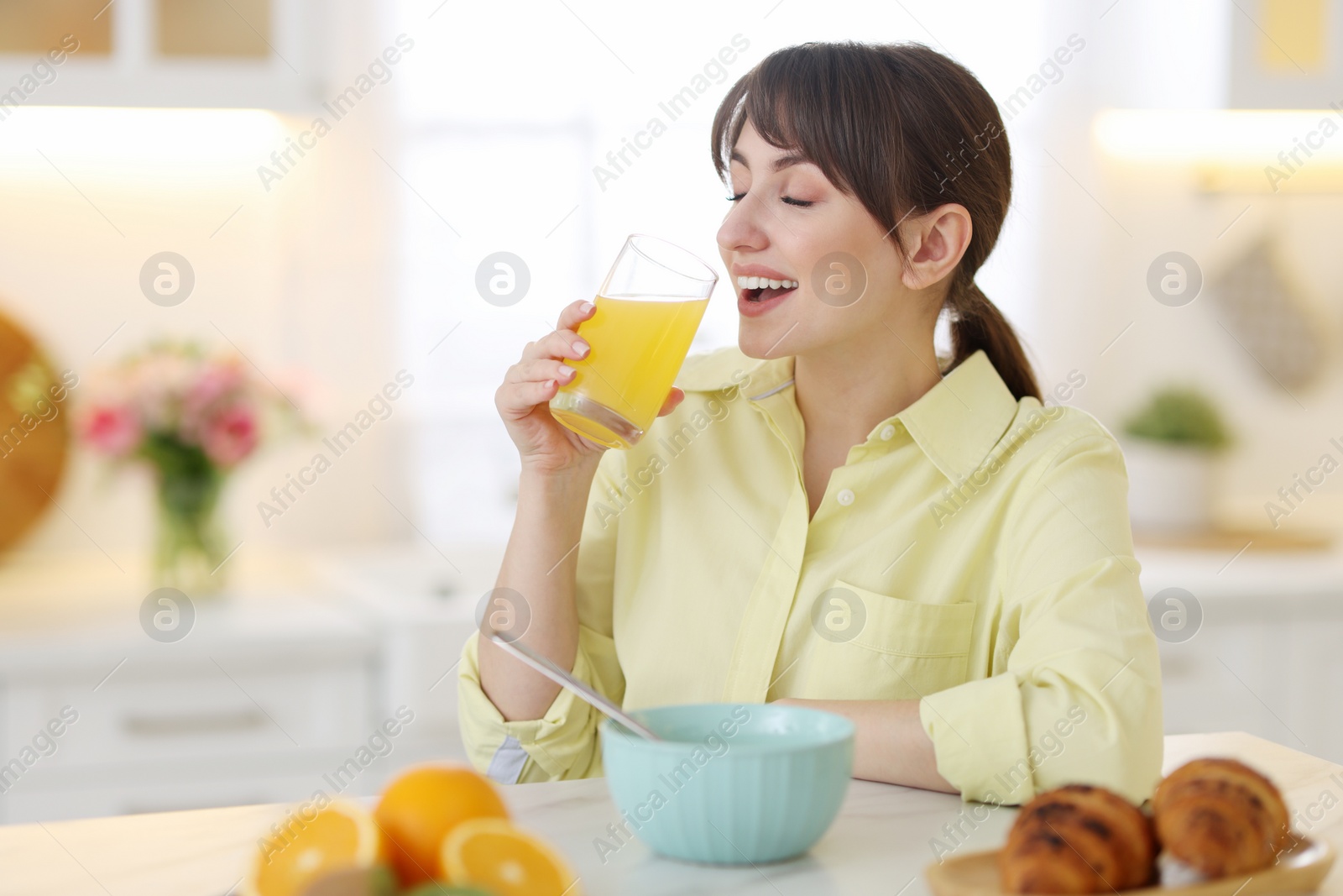 Photo of Smiling woman drinking juice at breakfast indoors