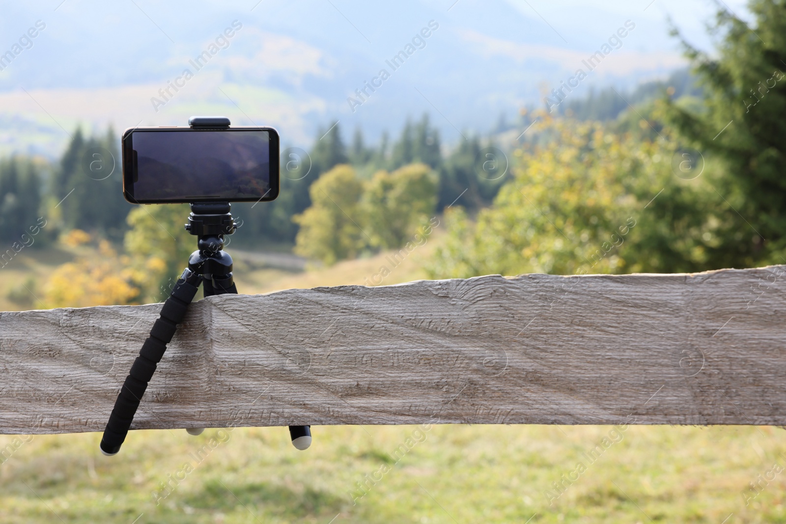 Photo of Tripod with smartphone outdoors. Space for text