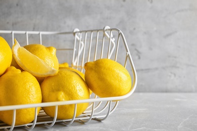 Photo of Metal basket with ripe lemons on table against light background