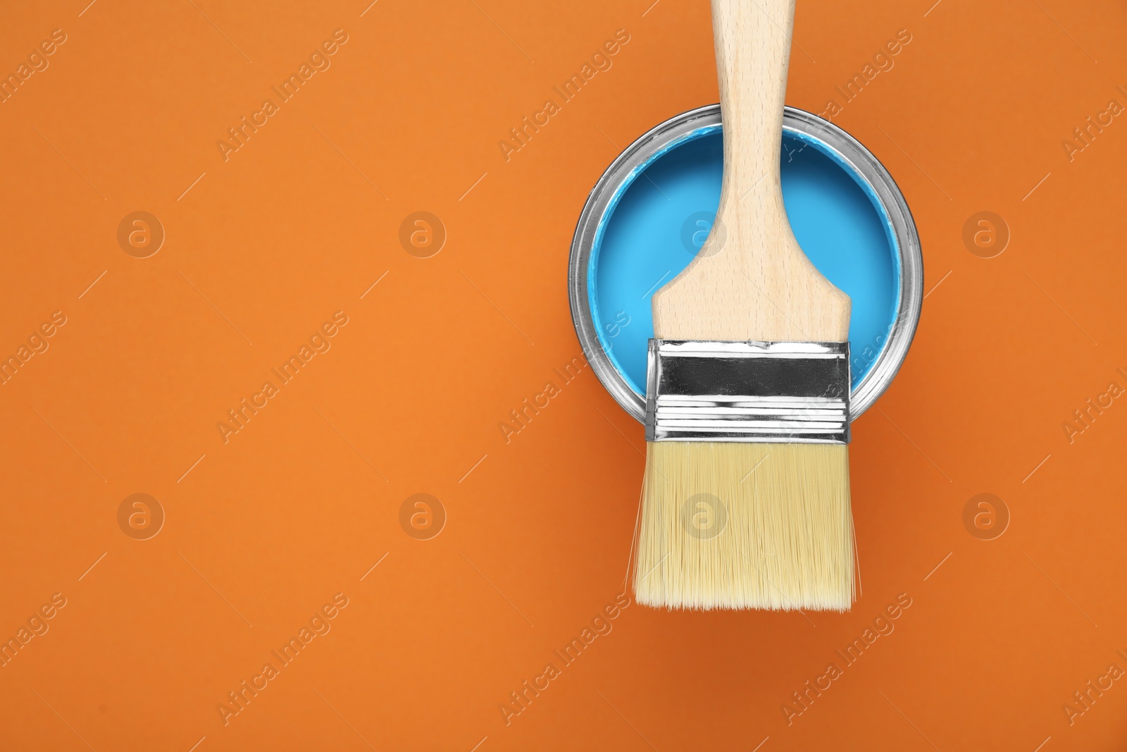 Photo of Can of light blue paint with brush on pale orange background, top view. Space for text