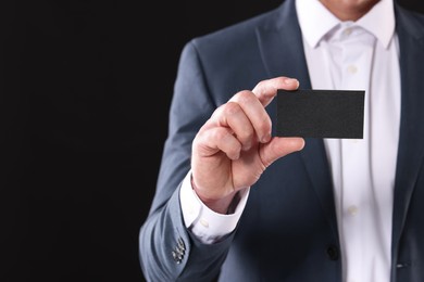 Photo of Businessman holding blank business card on black background, closeup. Space for text