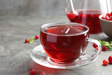 Photo of Tasty hot cranberry tea in glass cup and fresh berries on light grey textured table