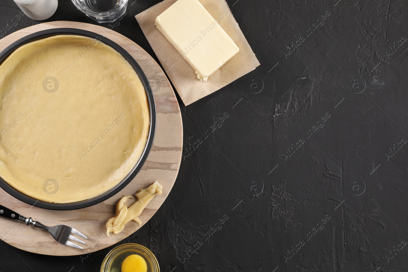 Photo of Making quiche. Pie tin with fresh dough and ingredients on black table, flat lay. Space for text