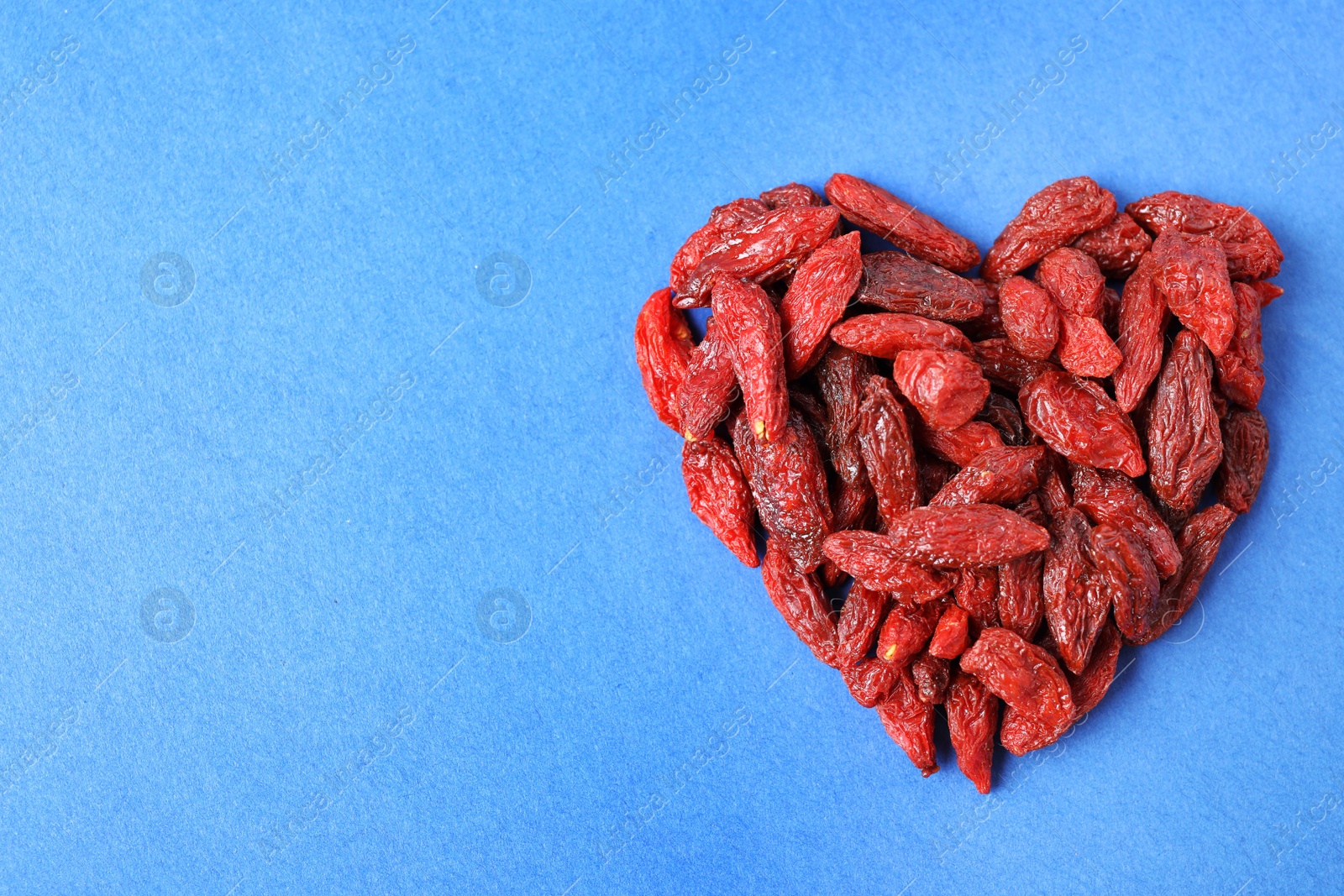 Photo of Heart of dried goji berries on blue background, top view. Space for text