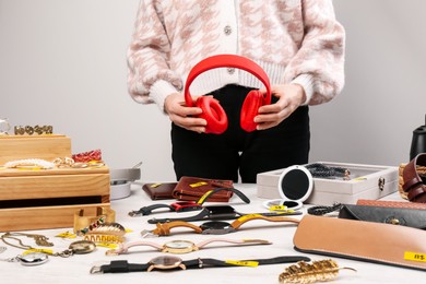Photo of Woman holding headphones near table with different stuff indoors, closeup. Garage sale
