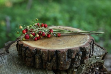 Bunch with tasty wild strawberries on wooden stump outdoors