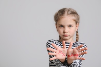 Girl showing hands with phrase Stop Bullying on light grey background, selective focus. Space for text