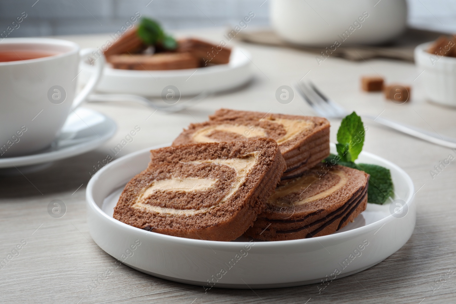 Photo of Tasty chocolate cake roll with cream and mint on light wooden table