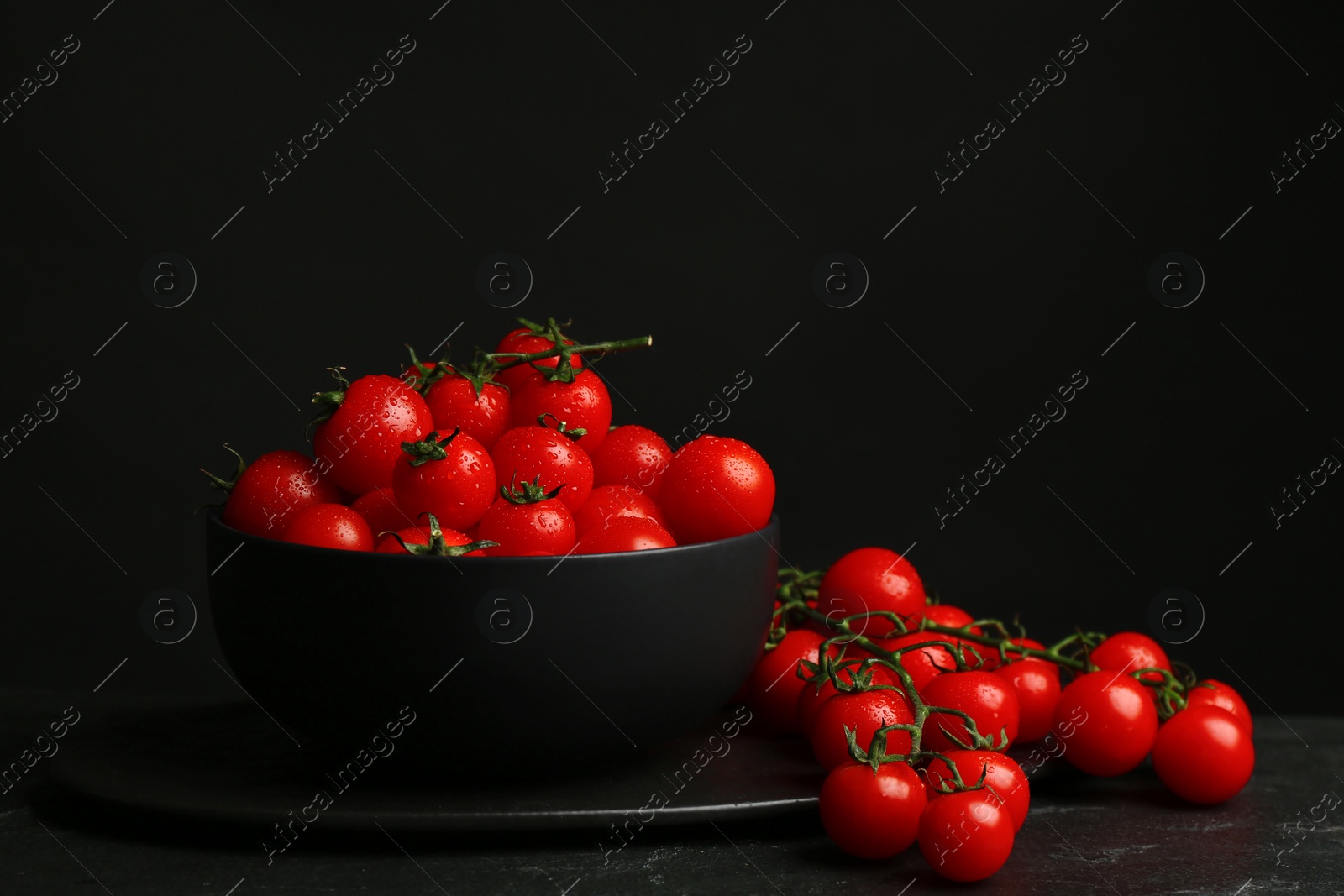 Photo of Fresh ripe cherry tomatoes with water drops on black table