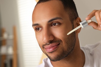 Handsome man applying cosmetic serum onto face in bathroom, closeup. Space for text