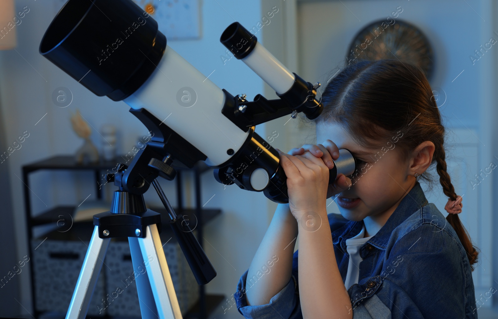 Photo of Cute little girl looking at stars through telescope in room