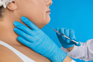 Photo of Woman with double chin getting injection on blue background, closeup. Cosmetic surgery