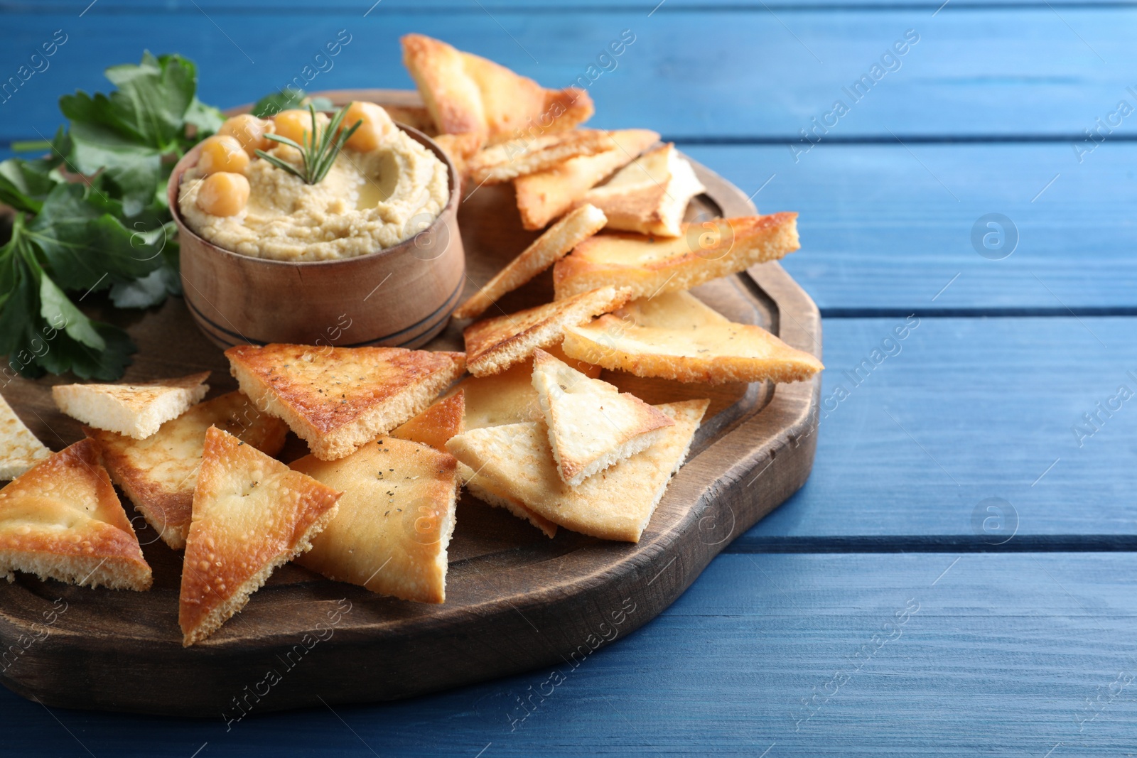 Photo of Delicious pita chips with hummus on blue wooden table, closeup