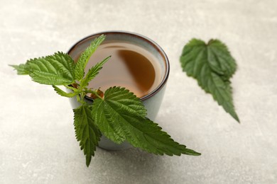 Cup of aromatic nettle tea with green leaves on light grey table