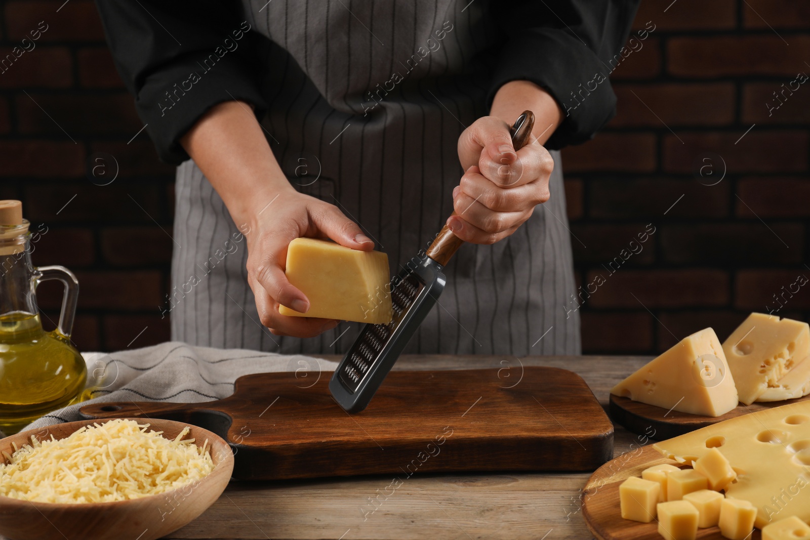 Photo of Woman grating cheese at wooden table, closeup