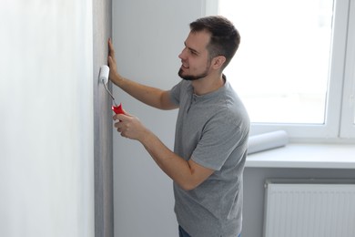 Man hanging stylish gray wallpaper in room