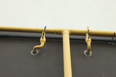 Photo of Yellow gas pipes with valves near brown wall outdoors