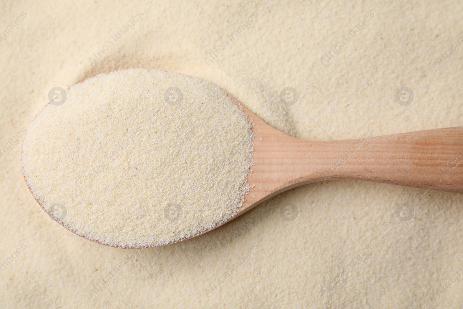 Photo of Uncooked organic semolina and wooden spoon, top view