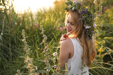 Photo of Young woman wearing wreath made of beautiful flowers outdoors on sunny day