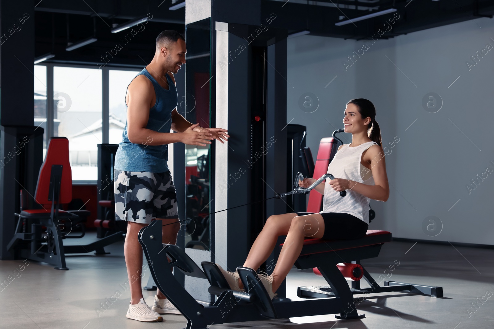 Photo of Happy trainer explaining woman how to do exercise properly in modern gym