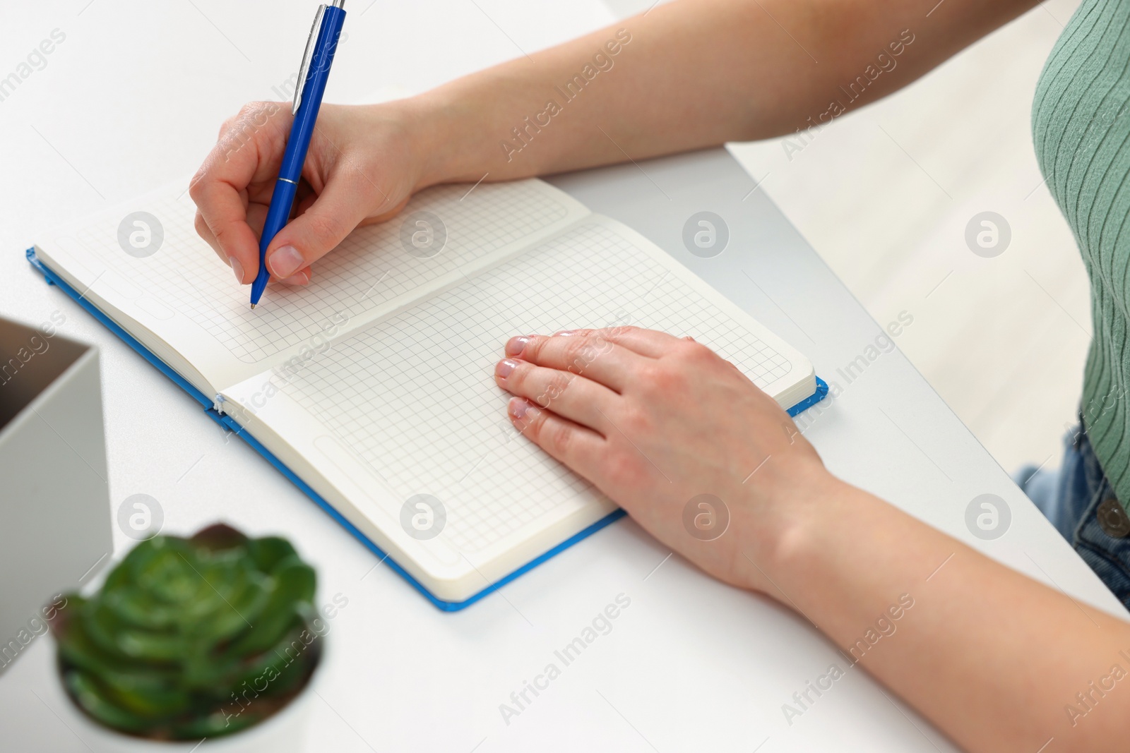 Photo of Young woman writing in notebook at white table, closeup