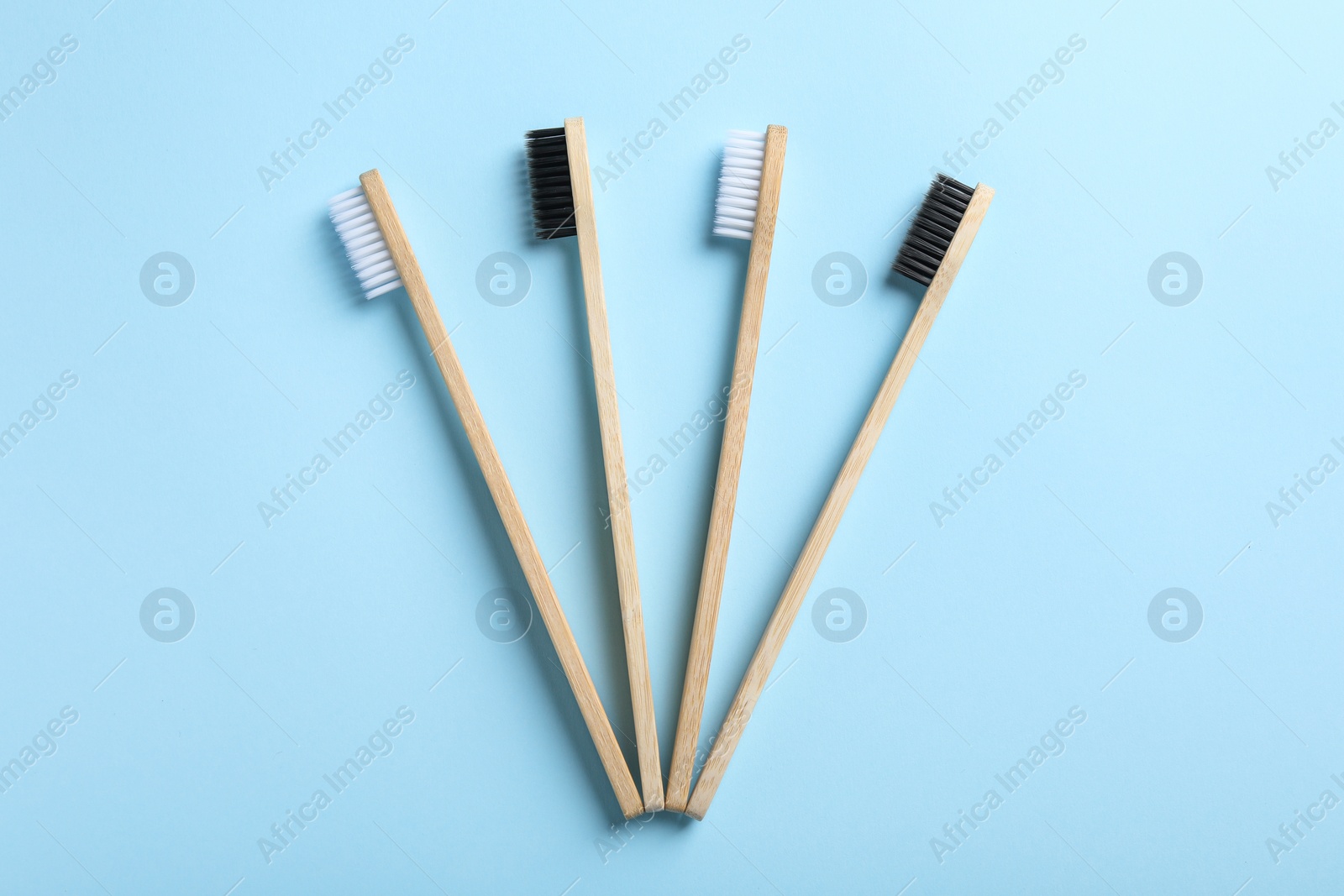 Photo of Bamboo toothbrushes on light blue background, flat lay