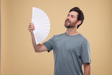 Man with hand fan suffering from heat on beige background