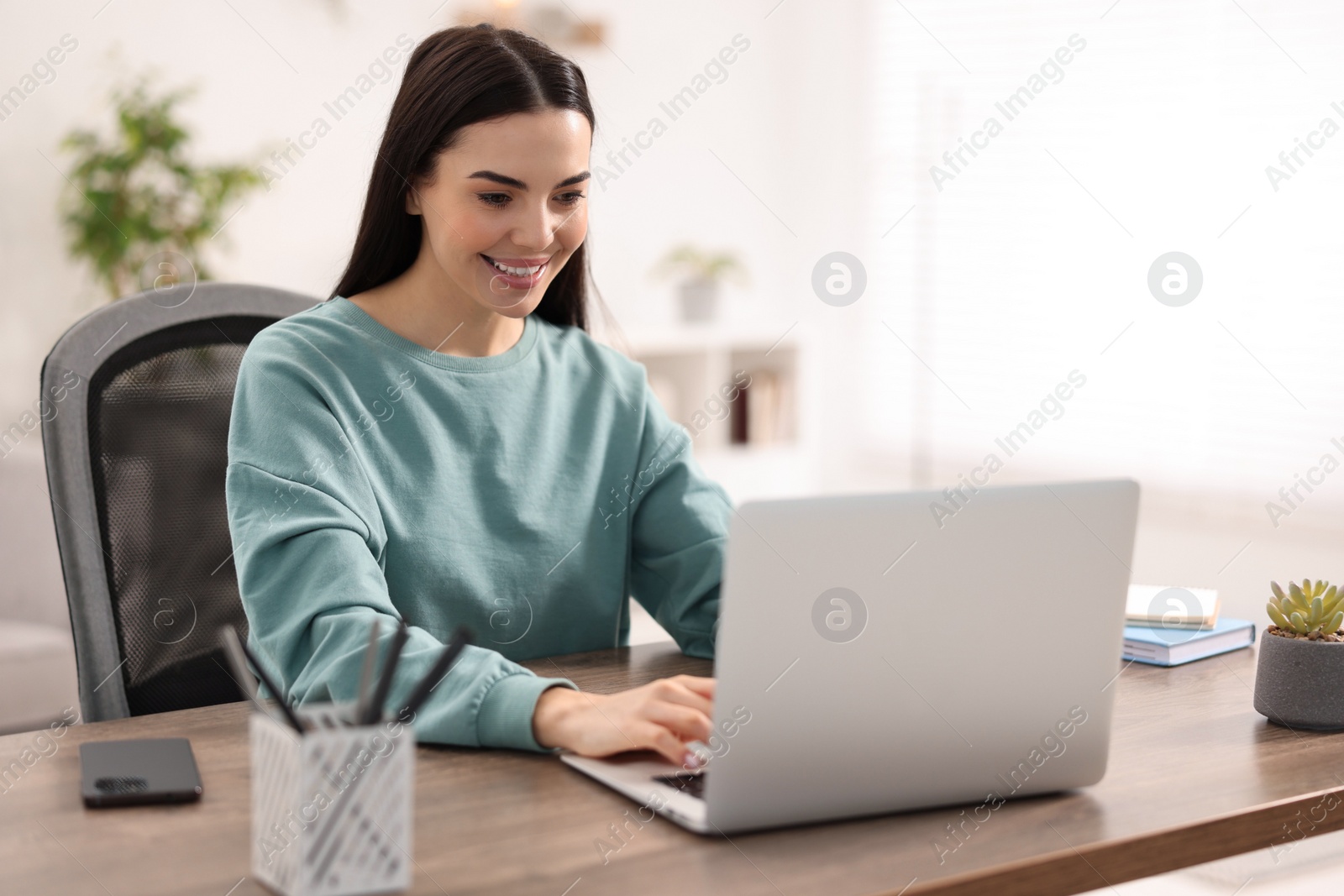 Photo of Young woman watching webinar at table in room