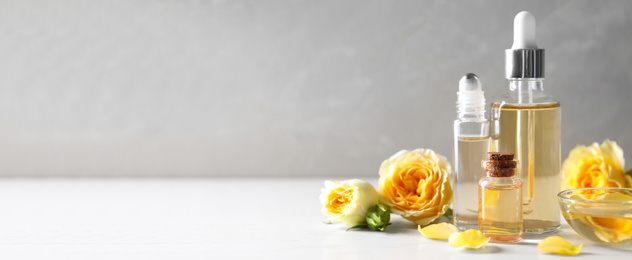 Bottles of rose essential oil and flowers on table, space for text. Banner design