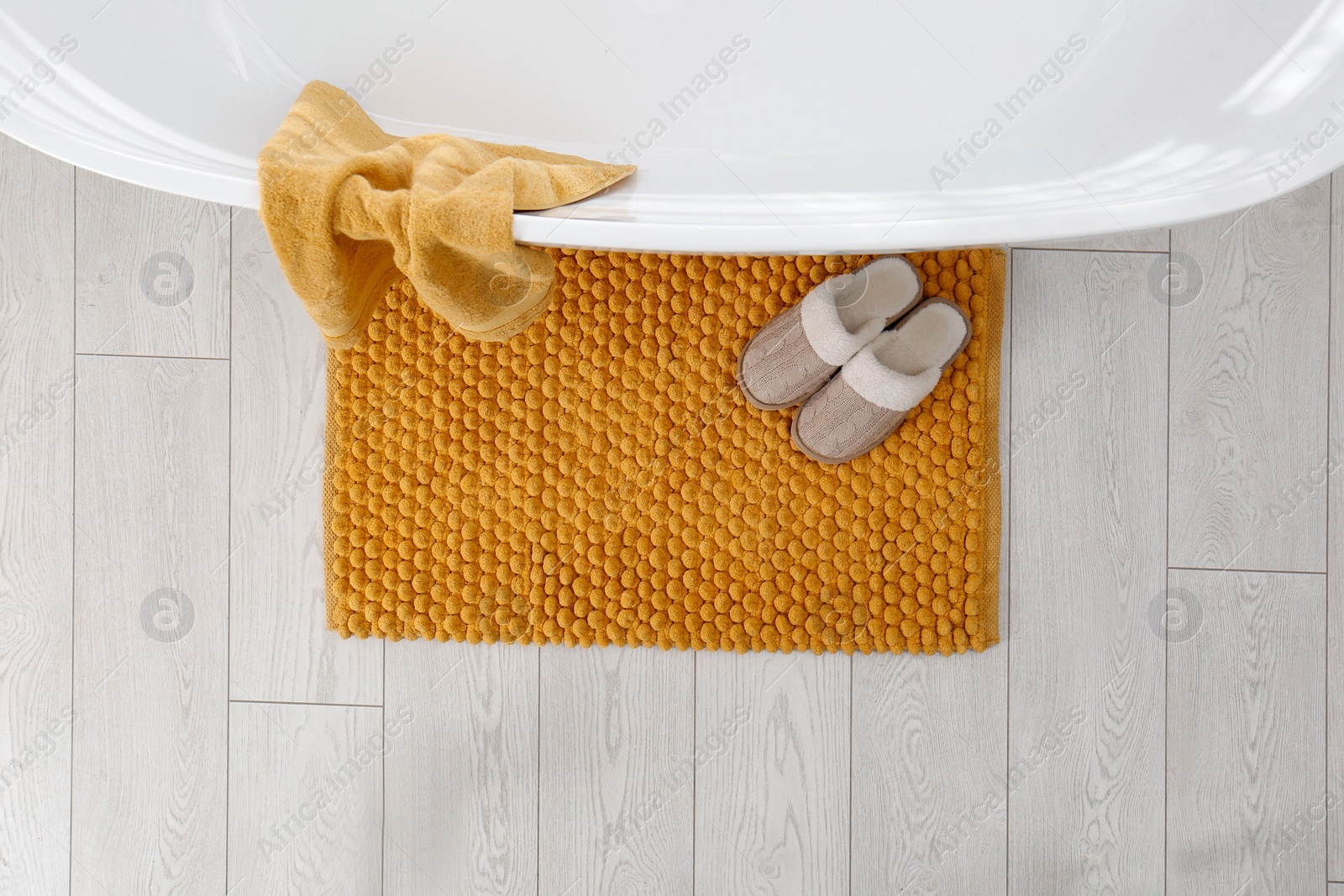 Photo of Soft orange bath mat and slippers on floor in bathroom, top view