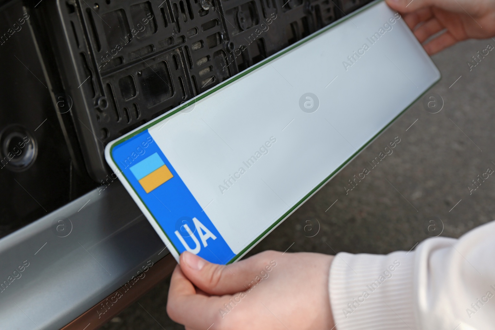 Photo of Woman installing vehicle registration plate outdoors, closeup