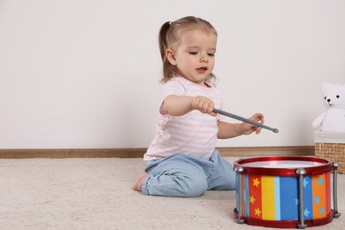 Photo of Cute little girl playing with drum and drumsticks at home, space for text