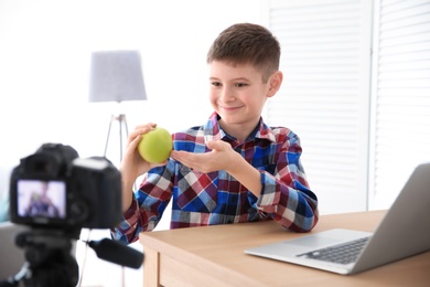 Photo of Cute little blogger with apple recording video at home