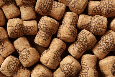 Many corks of wine bottles with grape images as background, top view