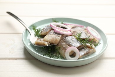 Plate with sliced salted herring fillet, onion rings and dill on white wooden table