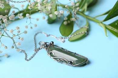 Photo of Beautiful silver necklace with nephrite gemstone and flowers on light blue background