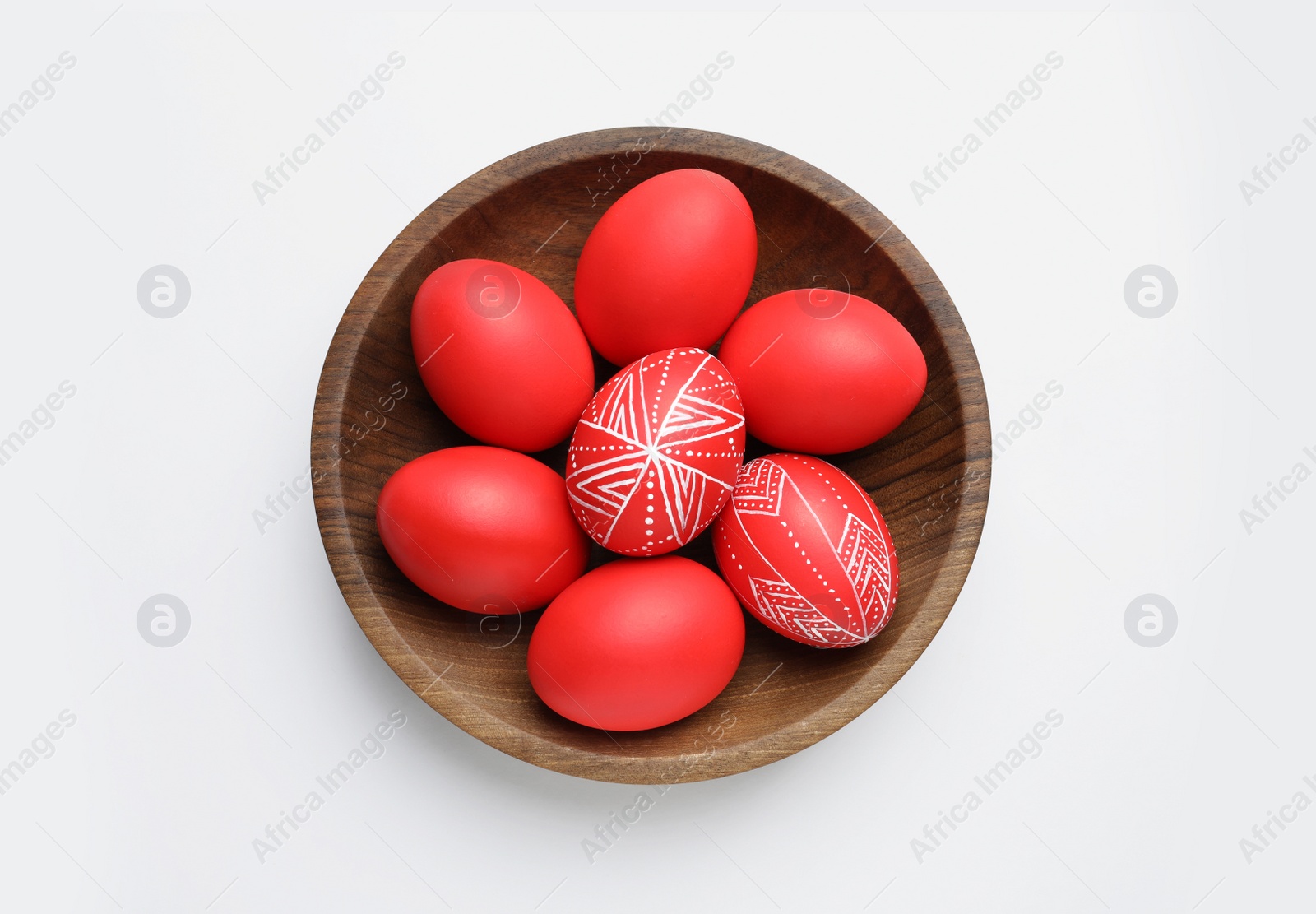 Photo of Wooden bowl with painted red Easter eggs on white background, top view