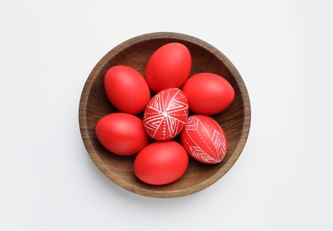 Photo of Wooden bowl with painted red Easter eggs on white background, top view