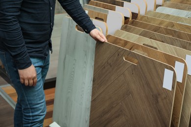 Photo of Man choosing wooden flooring among different samples in shop, closeup