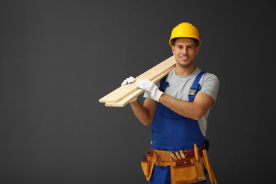 Handsome carpenter with wooden planks on dark background