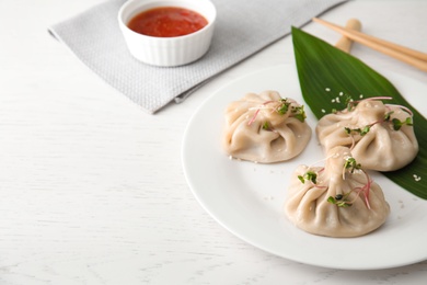 Plate with tasty baozi dumplings on white wooden table. Space for text