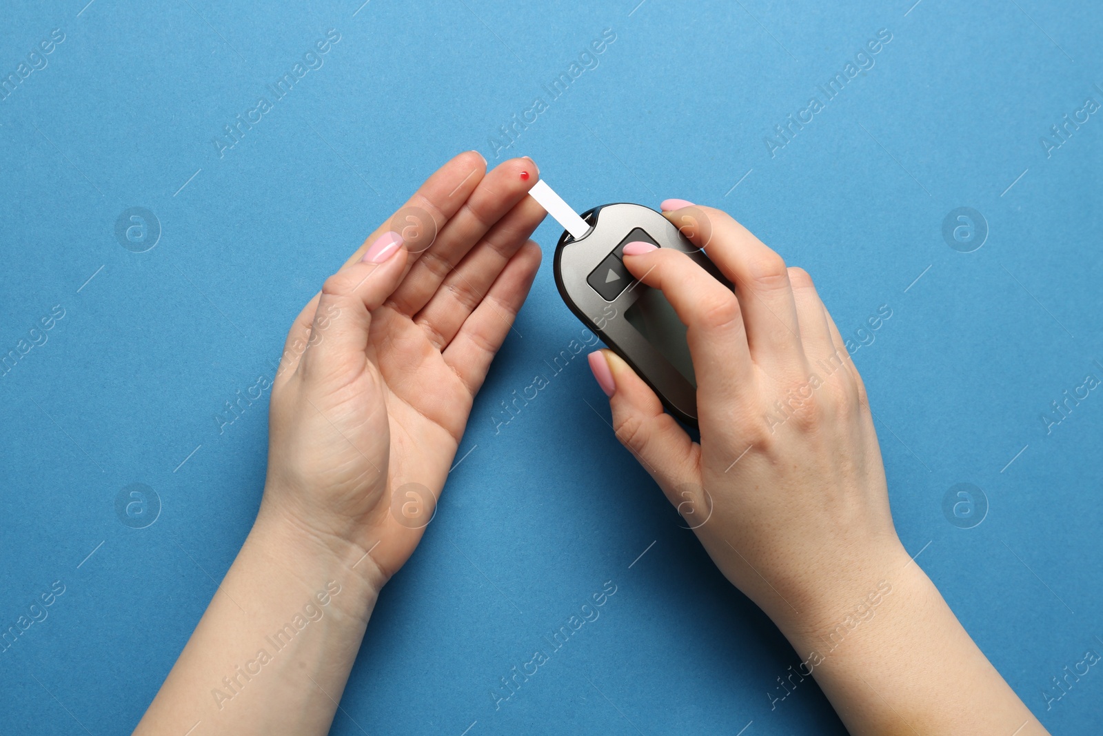 Photo of Diabetes. Woman checking blood sugar level with glucometer on light blue background, top view