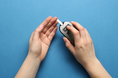 Diabetes. Woman checking blood sugar level with glucometer on light blue background, top view