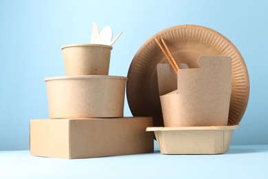 Photo of Eco friendly food packaging. Paper containers and tableware on white table against light blue background