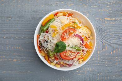 Photo of Tasty cooked rice noodles with vegetables on grey wooden table, top view