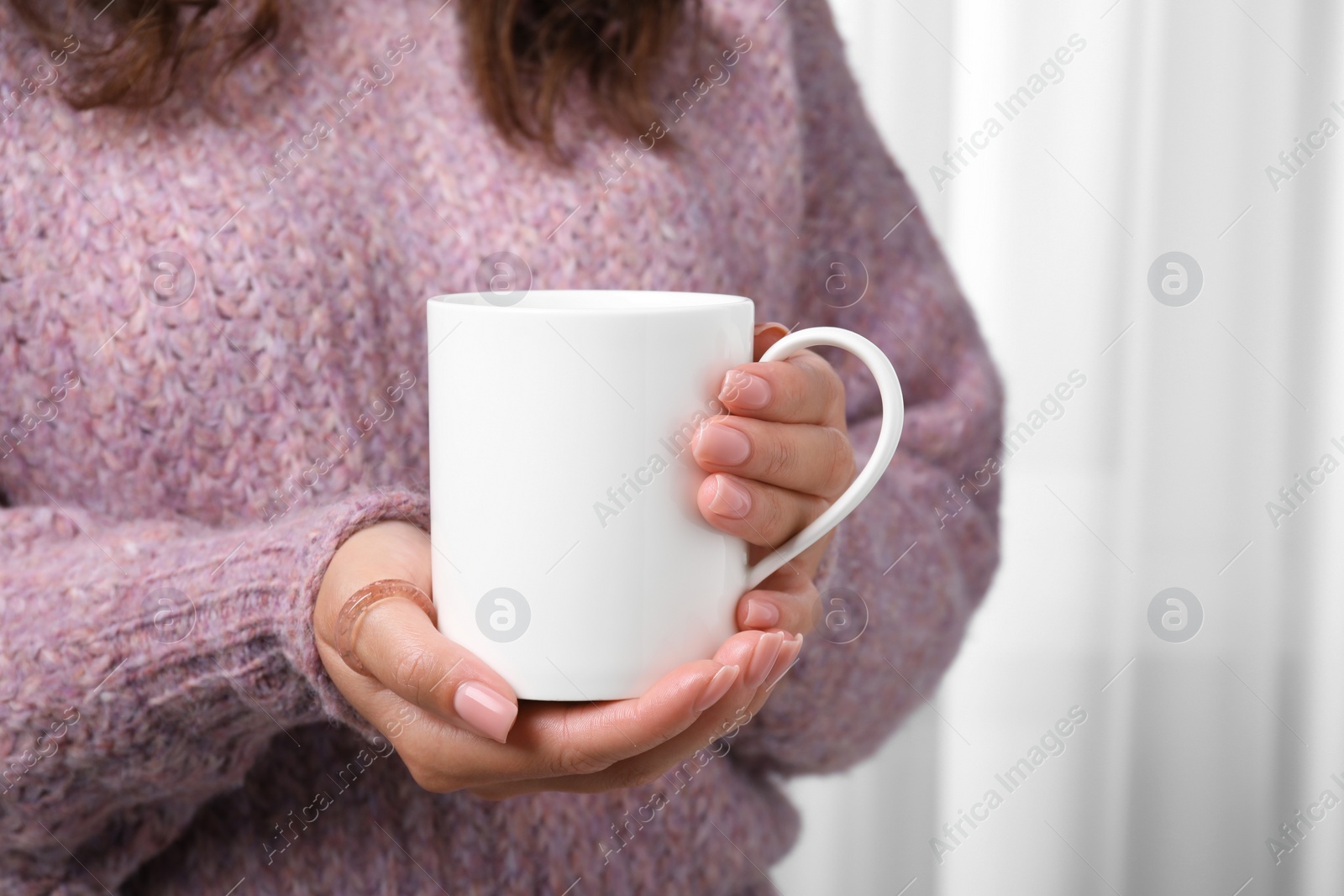 Photo of Woman holding white mug indoors, closeup. Mockup for design