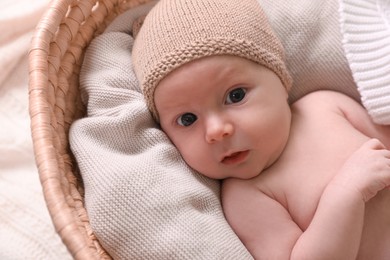 Photo of Cute newborn baby on white blanket in wicker crib, closeup